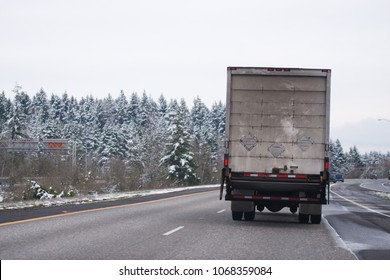Powerful middle size white day cab American made big rig semi truck with box cargo dry van trailer transporting industrial cargo and running on the wide multiline highwayIn winter snow weather 