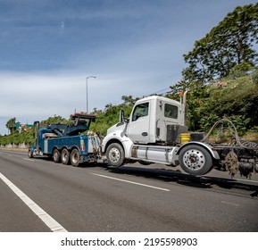 Powerful mobile helper heavy duty blue big rig towing semi truck tractor with extended arrow tow out of service elevated broken semi truck to auto repair shop running on the highway road - Shutterstock ID 2195598903