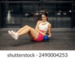 Powerful muscular female weightlifter in shape doing russian twist workout with kettlebell on a gym floor.