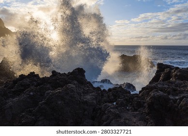 Powerful ocean wave exploding against dark volcanic rocks during sunset on the coast of Tenerife, Canary Islands, Spain.
