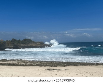 Powerful ocean waves crashing against rocky cliffs on a bright sunny day, with lush greenery in the background under a vivid blue sky. - Powered by Shutterstock