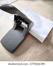 A powerful office hole punch with a stack of white paper on a table