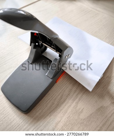 A powerful office hole punch with a stack of white paper on a table