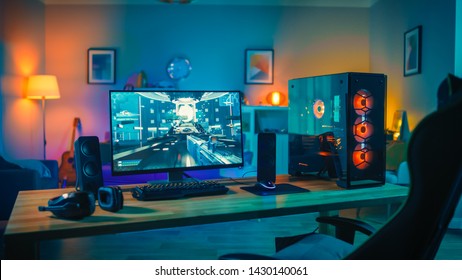 Powerful Personal Computer Gamer Rig with First-Person Shooter Game on Screen. Monitor Stands on the Table at Home. Cozy Room with Modern Design is Lit with Warm and Neon Light.