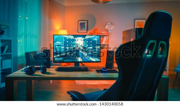 Powerful Personal\
Computer Gamer Rig with First-Person Shooter Game on Screen.\
Monitor Stands on the Table at Home. Cozy Room with Modern Design\
is Lit with Warm and Neon\
Light.