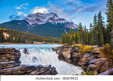 Powerful picturesque waterfall Athabasca. Pyramidal mountain covered with the first snow. Canada, Jasper National Park
