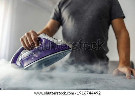 Powerful professional photo effect of water vapor from the hot iron. A modern lifestyle concept, a man who irons clothes at home