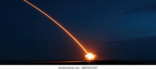 A powerful rocket ascends into the dark night sky, leaving a brilliant orange and yellow fiery trail behind it.