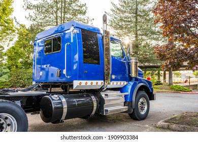 Powerful Shiny Big Rig Semi Truck Tractor In Blue With Painted Aluminum Fuel Tanks And Steps And Back Cab Compartment For Truck Driver Rest Standing On The Parking Lot In Sunshine