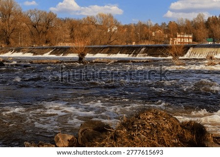 Powerful spring water thundering over a concrete dam. Wide river context, dense mist, and unstoppable force. Ideal for environment, engineering, or weather visuals.