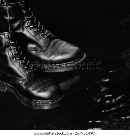 A powerful and stark black and white studio shot of a classic pair of boots, isolated on a pure black background. The monochrome treatment emphasizes the iconic design.