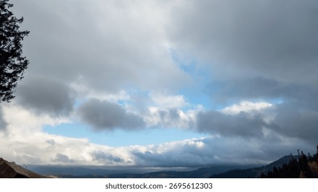 Powerful storm front with dark clouds contrasting blue sky over a rural village in autumnal mountains, capturing natures drama and seasonal beauty in a scenic valley.