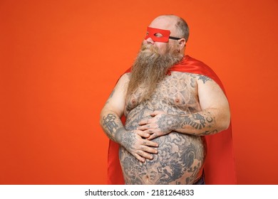 Powerful Strong Fat Chubby Overweight Tattooed Bearded Man Dressed In Red Superhero Suit Have Supernatural Abilities Stroking Belly Isolated On Orange Backround Studio Portrait Real Heroes Defend You.