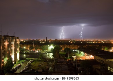 Powerful thunderbolt hits the city at night. A strong lightning strike over a dark gray sky hits the ground, illuminating the industrial area around