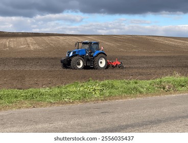 A powerful tractor cultivates the land in the field, preparing the soil for sowing. The bright landscape and clear sky add harmony to the scene. - Powered by Shutterstock