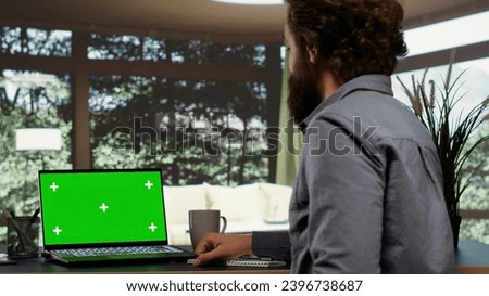 Powerful tycoon relaxes at his impressive mansion in a forest, looking at greenscreen on personal computer. Global enterprise chairman connects on laptop with blank copyspace, wealthy lifestyle.