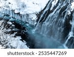 A powerful waterfall cascading over icy cliffs into a partially frozen river, surrounded by snow.