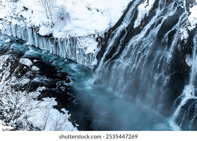 A powerful waterfall cascading over icy cliffs into a partially frozen river, surrounded by snow. - Powered by Shutterstock