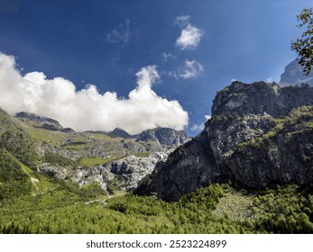 A powerful waterfall descends from a steep, rocky cliff, surrounded by patches of green vegetation and rugged rock formations. - Powered by Shutterstock