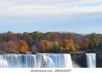 A powerful waterfall dropping over a cliff edge with autumn trees on top