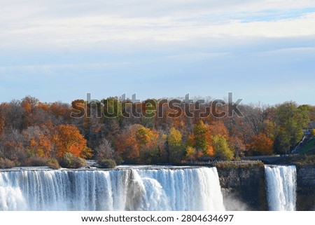 A powerful waterfall dropping over a cliff edge with autumn trees on top