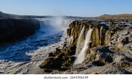 A powerful waterfall flows dramatically over rugged cliffs at Dettifoss, one of Icelands most breathtaking natural wonders. The sound of rushing water echoes in the serene landscape.