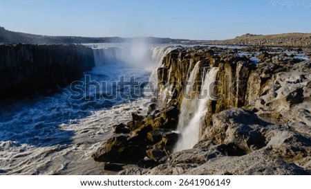 A powerful waterfall flows dramatically over rugged cliffs at Dettifoss, one of Icelands most breathtaking natural wonders. The sound of rushing water echoes in the serene landscape.