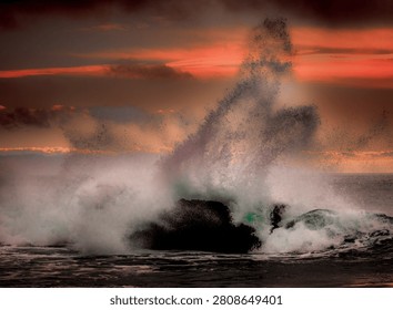 A powerful wave explodes into a mist of spray as it collides with a solitary rock formation during a vibrant sunset over the sea