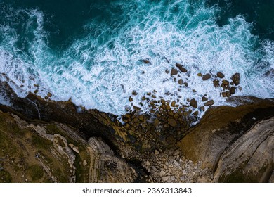 The powerful waves crash against the cliff's base, creating a mesmerizing display of nature's force. Ideal for themes of nature, adventure, travel, and coastal landscapes