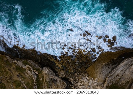 The powerful waves crash against the cliff's base, creating a mesmerizing display of nature's force. Ideal for themes of nature, adventure, travel, and coastal landscapes