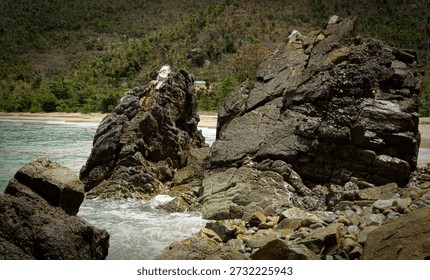 Powerful waves crash dramatically against a rugged rock in the turquoise waters of the Caribbean Sea, sending white spray into the air. The contrast between the deep blue sea, foaming waves, and dark textured rock creates a striking and dynamic coastal scene. Sunlight reflects off the water, highlighting the movement and energy of the waves as they collide with the sturdy rock formation.

The scene captures the raw power and beauty of the Caribbean coastline, showcasing both the force of nature and the vibrant colors of the tropical ocean. Ideal for stock photo themes such as coastal landscapes, ocean waves, natural energy, tropical nature, adventure, and outdoor exploration. This image conveys movement, strength, and the untamed beauty of the seaside environment.