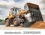 Powerful wheel loader or bulldozer isolated on sky background. Loader pours crushed stone or gravel from the bucket. Powerful modern equipment for earthworks and bulk handling