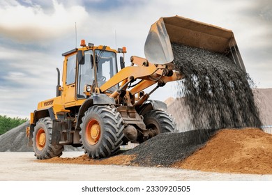 Powerful wheel loader or bulldozer isolated on sky background. Loader pours crushed stone or gravel from the bucket. Powerful modern equipment for earthworks and bulk handling