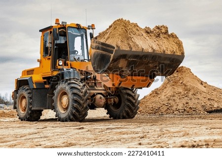 Powerful wheel loader or bulldozer working on a quarry or construction site. Loader with a full bucket of sand. Powerful modern equipment for earthworks