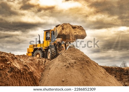 Powerful wheel loader or bulldozer working on a quarry or construction site. Loader with a full bucket of sand against the sky. Powerful modern equipment for earthworks
