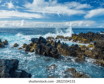 Powerful white ocean waves foaming and crashing into dark volcanic rock reefs near Porto Moniz natural pools, Madeira, Portugal.