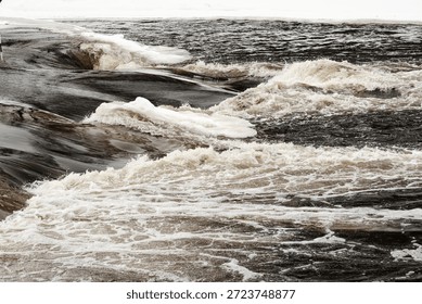 Powerful winter river rapids with floating ice sheets and turbulent dark water, capturing raw energy, motion and dramatic seasonal transition.