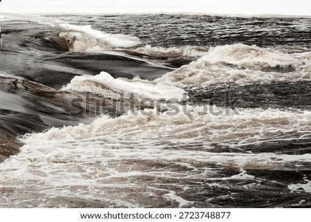 Powerful winter river rapids with floating ice sheets and turbulent dark water, capturing raw energy, motion and dramatic seasonal transition.