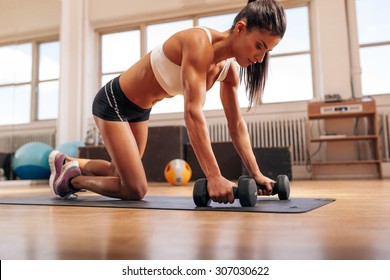 Powerful woman doing push-ups on dumbbells in gym. Muscular female exercising in health club.