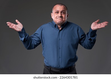 Powerless mature businessman with arms raised with an I can't do anything expression on his face, isolated on gray background