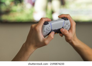 Poznan, Poland - August 2022. Man Play With Play Station 5 Dual Sense Controller In Front Of Blurred TV Screen At Home. Man's Hands Holding Modern Joystick And Playing Video Games On Gaming Console.