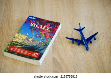 POZNAN, POLAND - Feb 20, 2022: A Lonley Planet Travel Guide About Sicily Laying Next To A Toy Model Passenger Plane On A Table 