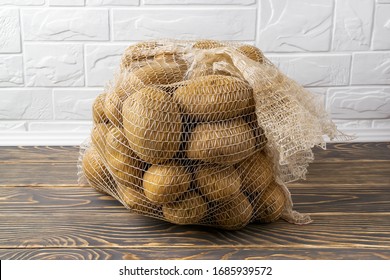 PP Mesh Bag With 10 Kg Of Farm Potatoes. Polypropylene Net Sack With 22 Lb Of Organic Potatoes On A Dark Wooden Floor. To Buy Fresh Vegetables In Bulk. Front View.