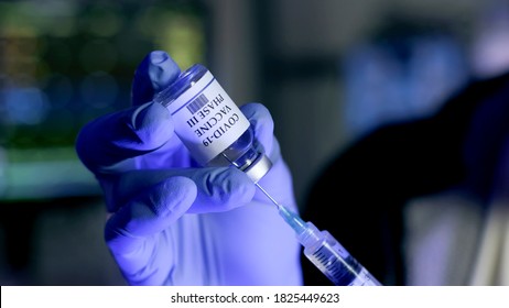 The PPE Covered Hand Of A Nurse Or Front Line Healthcare Worker Holding A Vial Of Vaccine For The Phase III Clinical Trials Against COVID-19. 