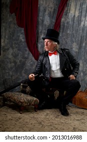Pportrait of victorian steampunk, looking away, wearing top hat, tail coat, bow tie and sitting on trunk.