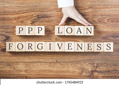 PPP LOAN FORGIVENESS Text On Wooden Blocks On Rustic Textured Background. Female Hand Holds Blocks. Small Business Paycheck Protection Program. Banking And Finance Concept