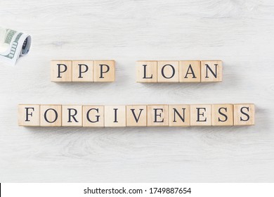 PPP LOAN FORGIVENESS Text On Wooden Blocks On Grey Wooden Background. US Dollars Roll. Small Business Paycheck Protection Program. Banking And Finance Concept