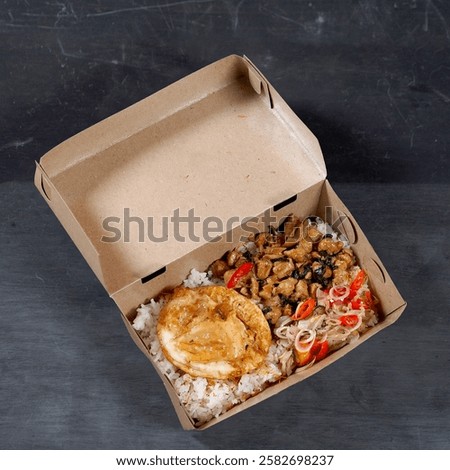 A practical box meal featuring white rice, savory spicy balado sausage, and a fried egg as a complement