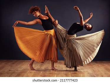 Practice and dedication make perfection. Two contemporary dancers with flowing skirts in front of a dark background.