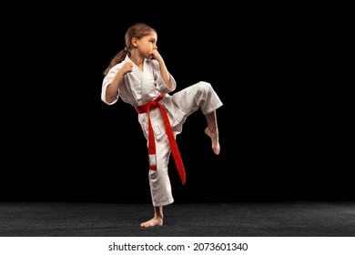 Practice. Karate, taekwondo girl with yellow belt isolated on dark background in neon light. Little female model, sport kid training in motion and action. Sport, movement, childhood concept.